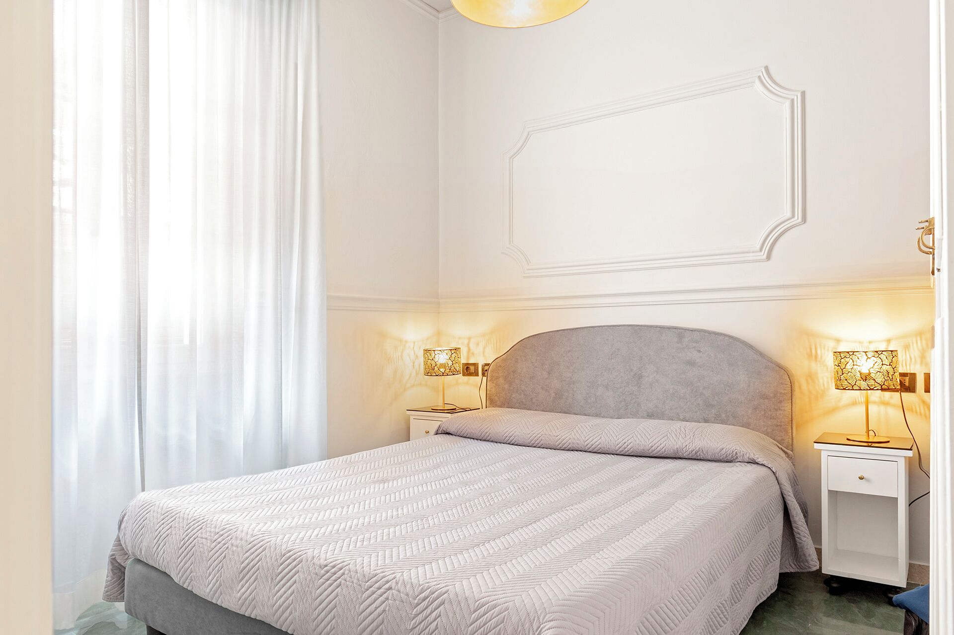 A neatly arranged bedroom with a bed, two bedside tables, and a wall-mounted light fixture.