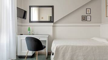 A hotel room with a bed, a desk with a chair, a TV mounted on the wall, and a window with curtains.