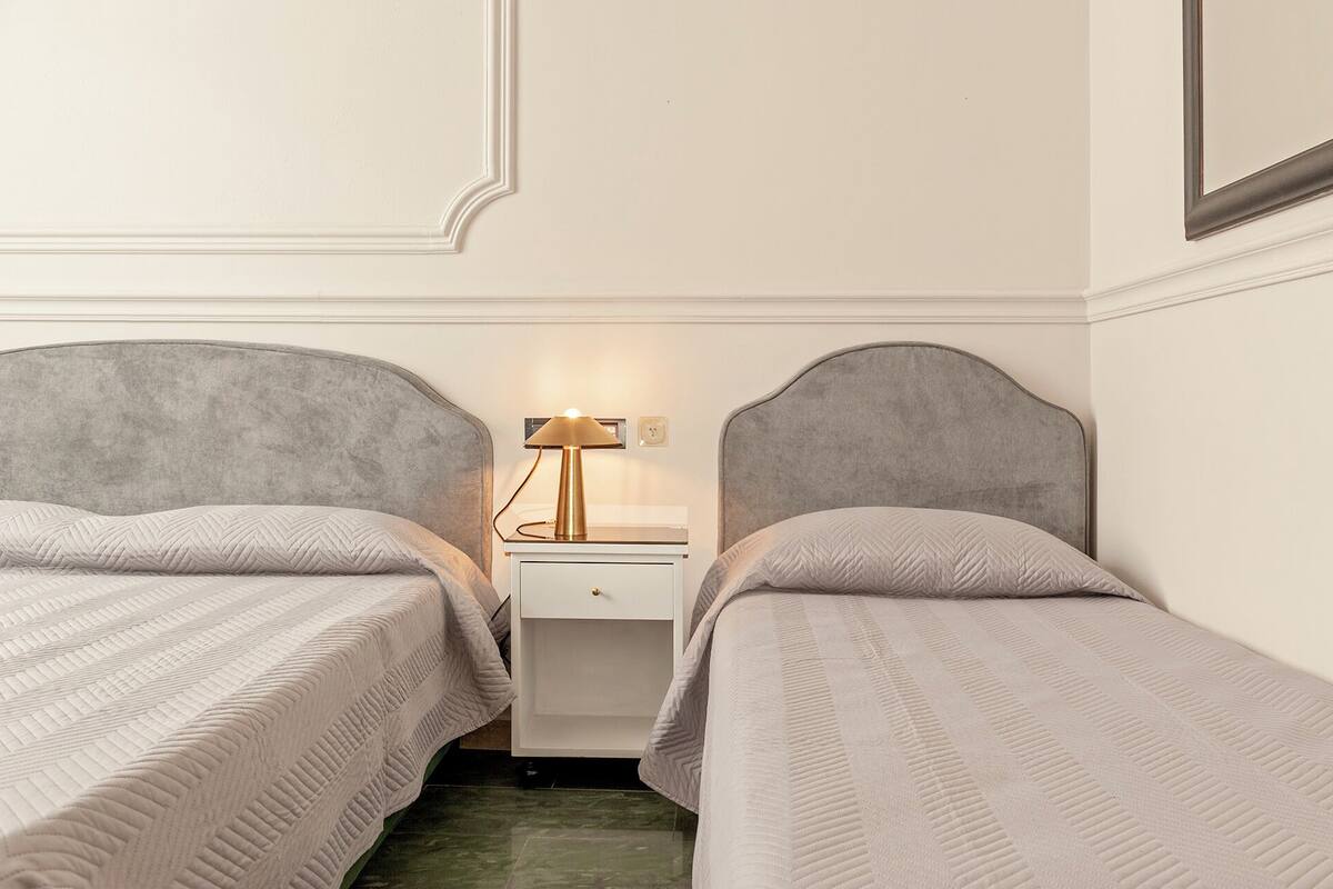 Ein Hotelzimmer mit zwei Betten, einem Nachttisch mit Lampe und einer kleinen Schublade.