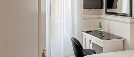 Habitación de hotel con cama, escritorio con televisor, silla y puerta con placa de número.