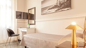 Een hotelkamer met een bed, een bureau, een stoel, een lamp en een schilderij aan de muur.