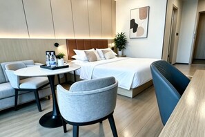 A modern hotel room with a bed, a round table, two chairs, a bench, and a wall-mounted artwork.