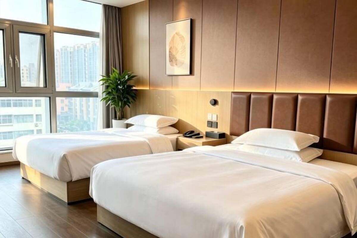 A hotel room with two beds, a nightstand, a plant, and a city view.
