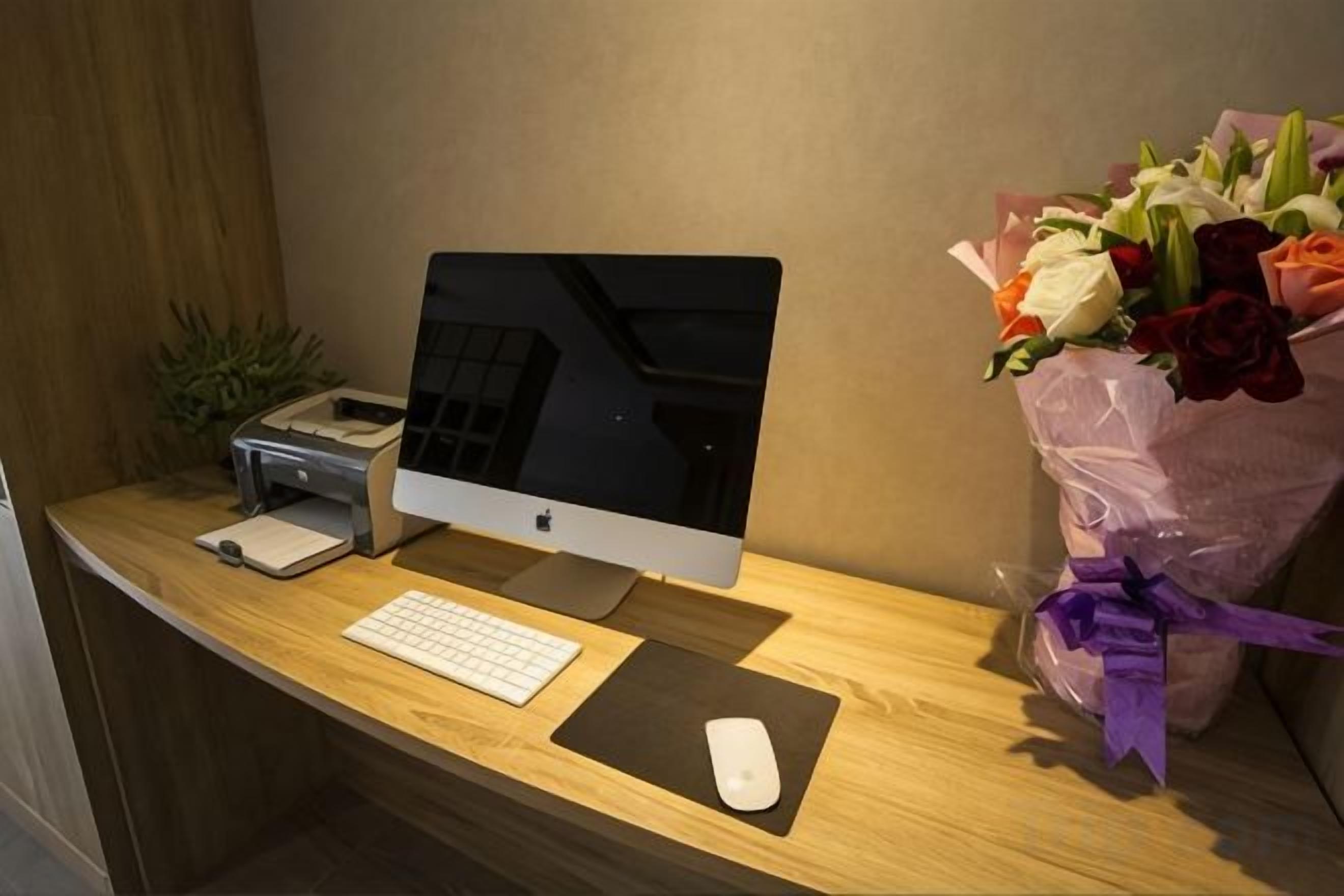A desk with a computer, keyboard, mouse, and a bouquet of flowers.