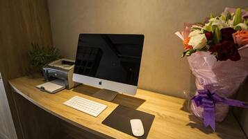 A desk with a computer, keyboard, mouse, and a bouquet of flowers.