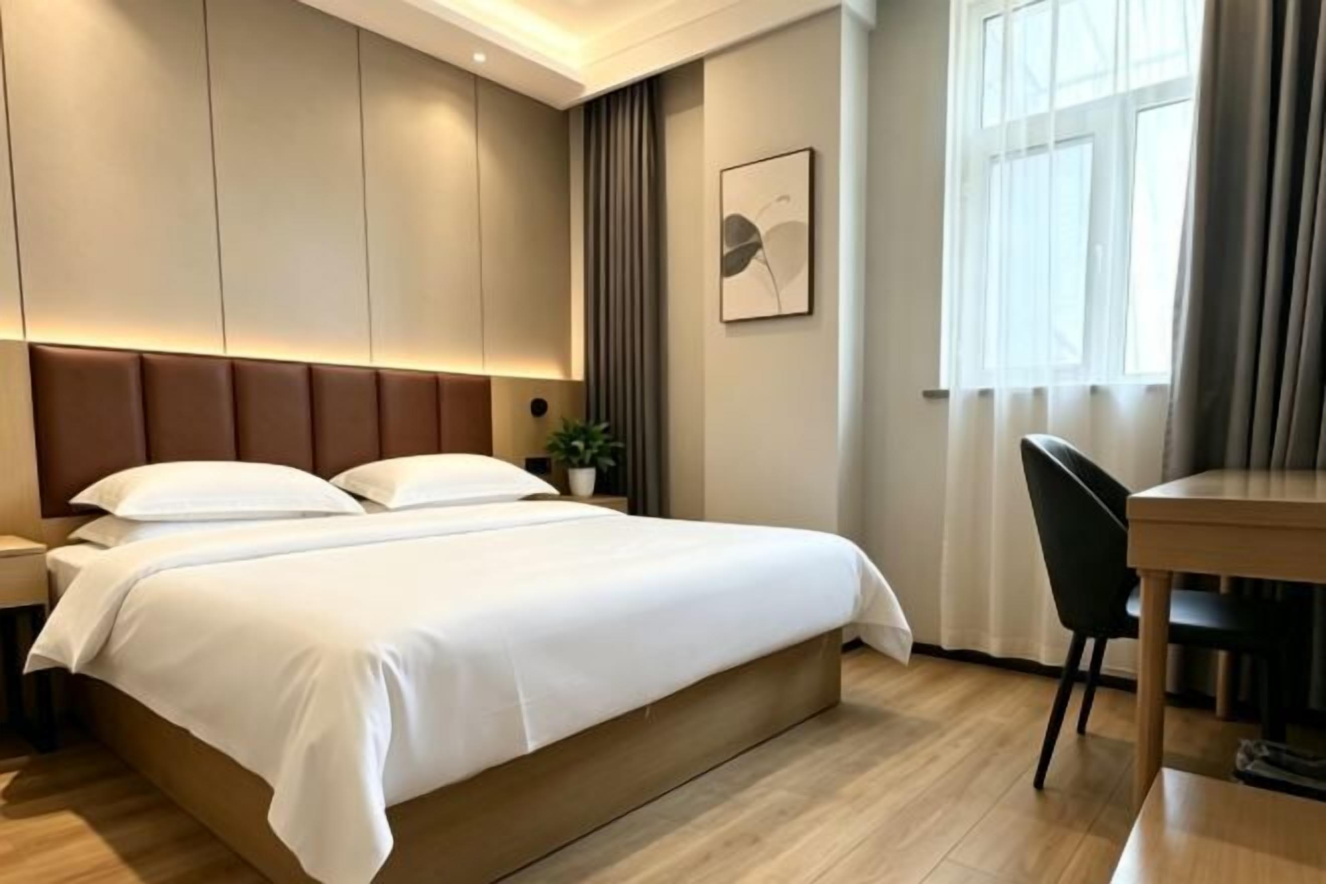 A hotel room with a bed, bedside table, lamp, and a window with curtains.