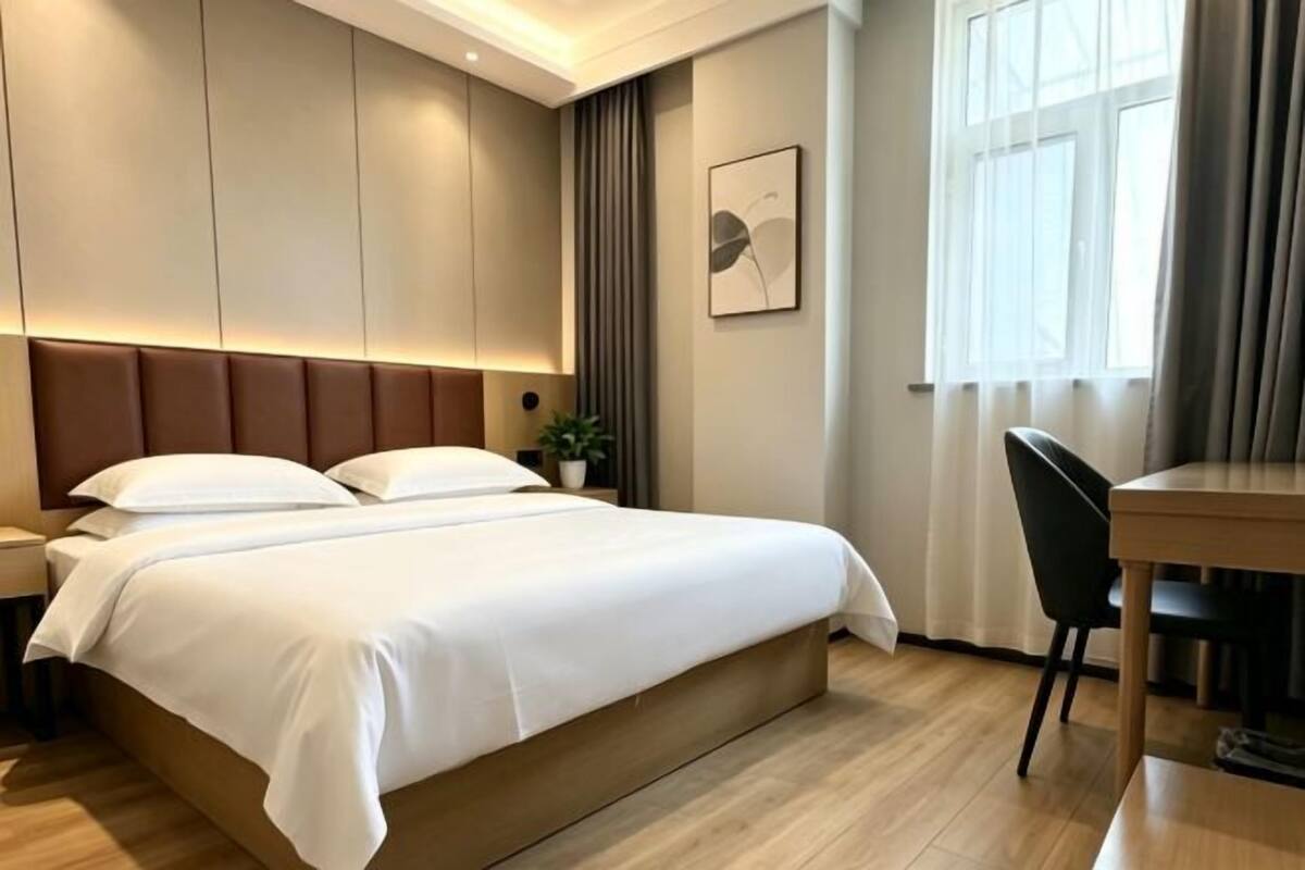 A hotel room with a bed, bedside table, lamp, and a window with curtains.