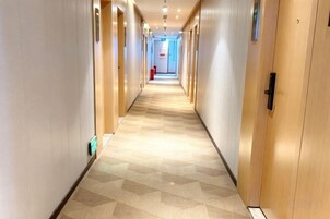 Un pasillo de hotel con puertas a ambos lados, una alfombra estampada y un extintor en la pared.