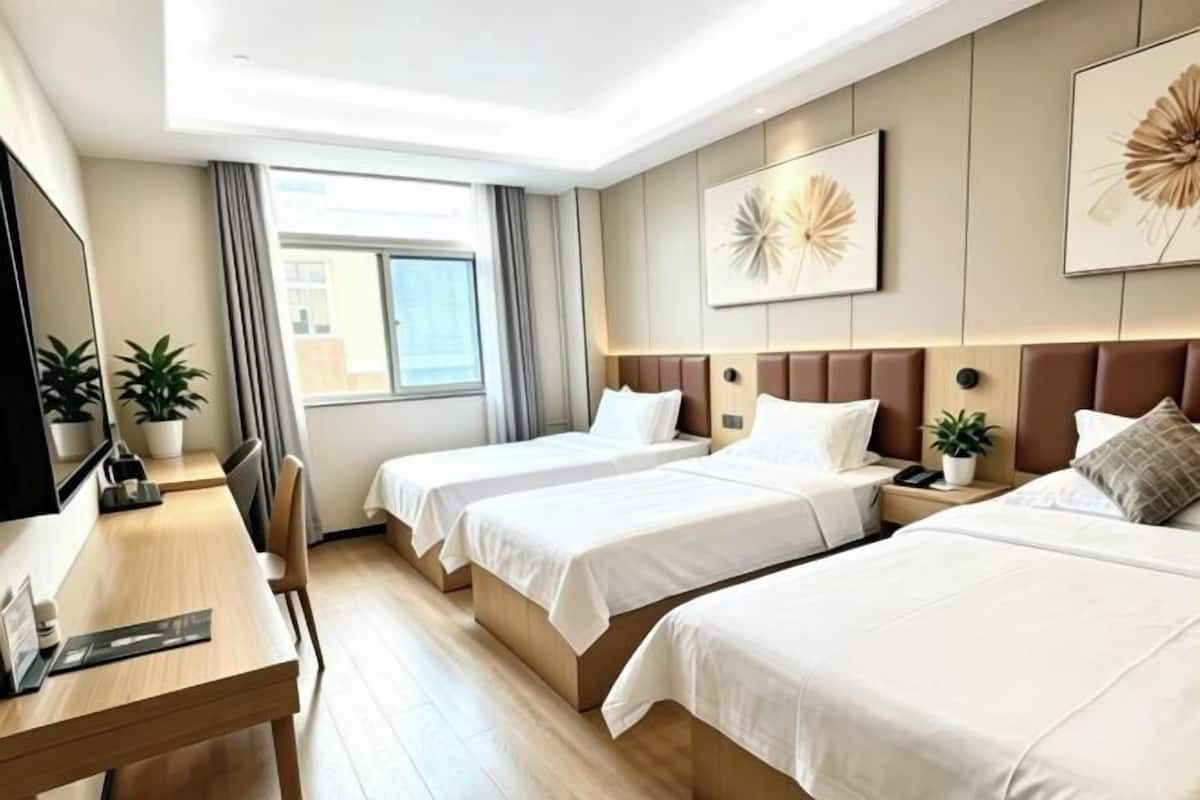 A hotel room with two beds, a desk, a TV, and a window with curtains.