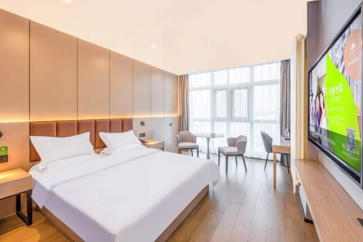 A hotel room with a large bed, bedside tables, a TV, a small table with chairs, and a large window.