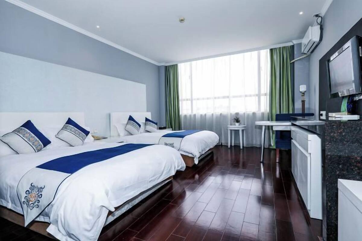 A hotel room with two beds, a desk, a TV, and a window with curtains.
