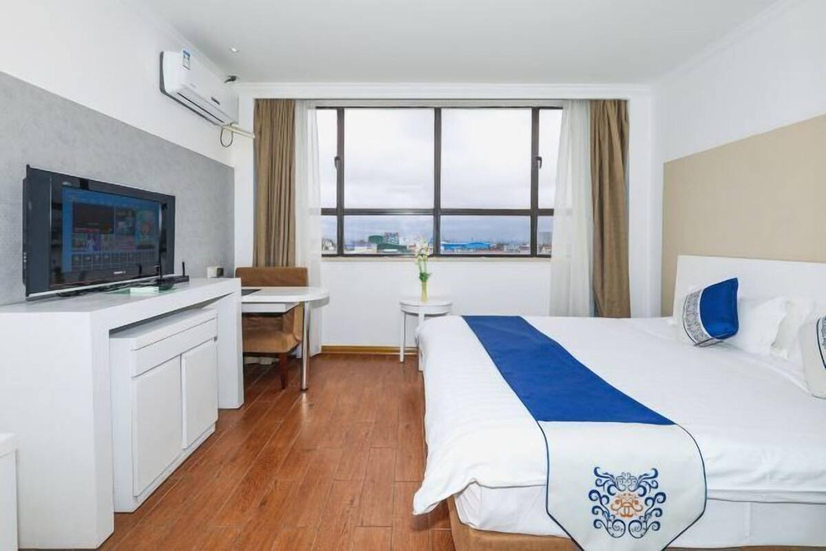 A hotel room with a bed, a desk, a chair, a TV, and a window with a city view.