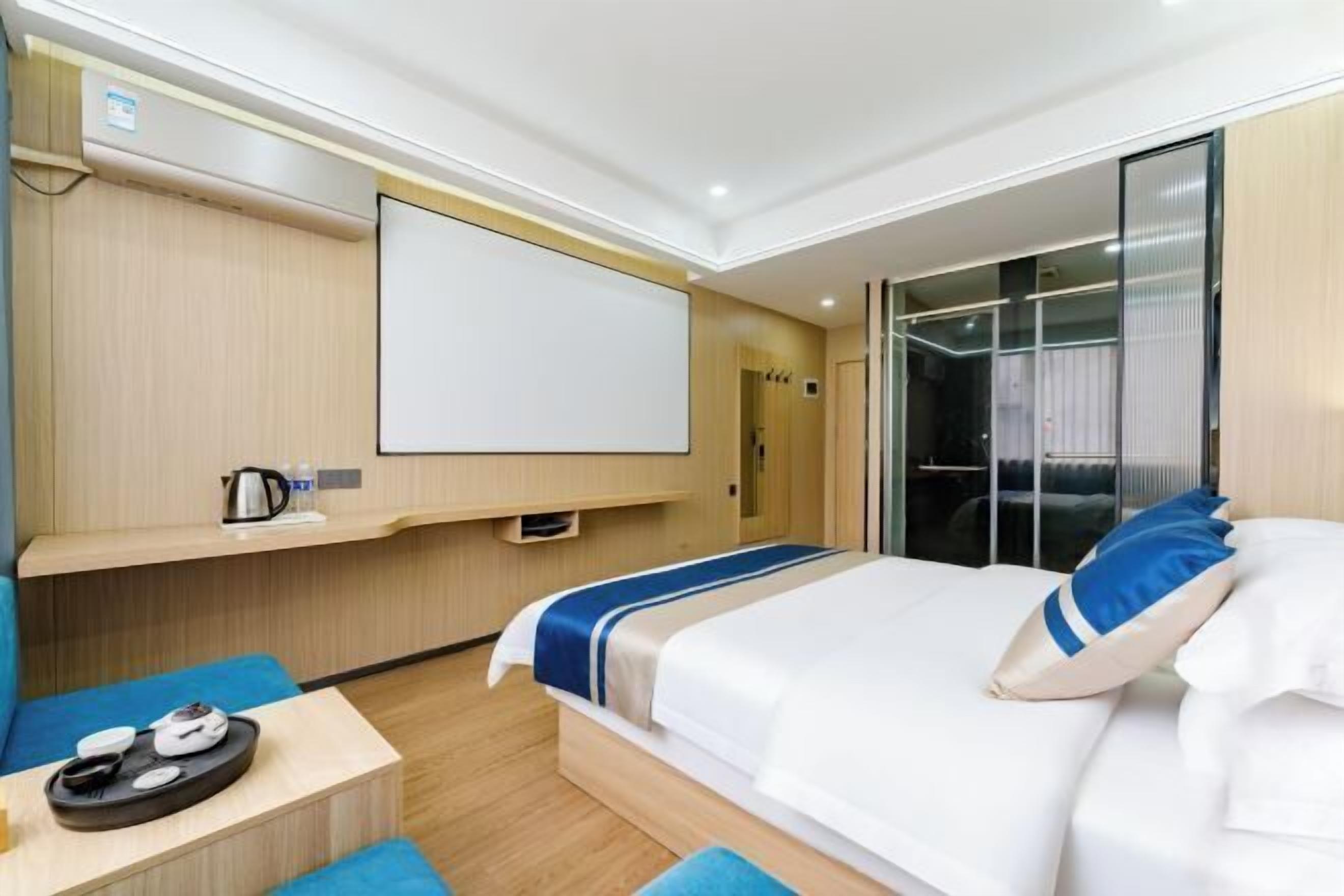 A modern hotel room with a bed, a desk with a kettle, and a large window.