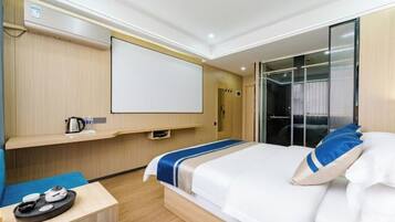 A modern hotel room with a bed, a desk with a kettle, and a large window.