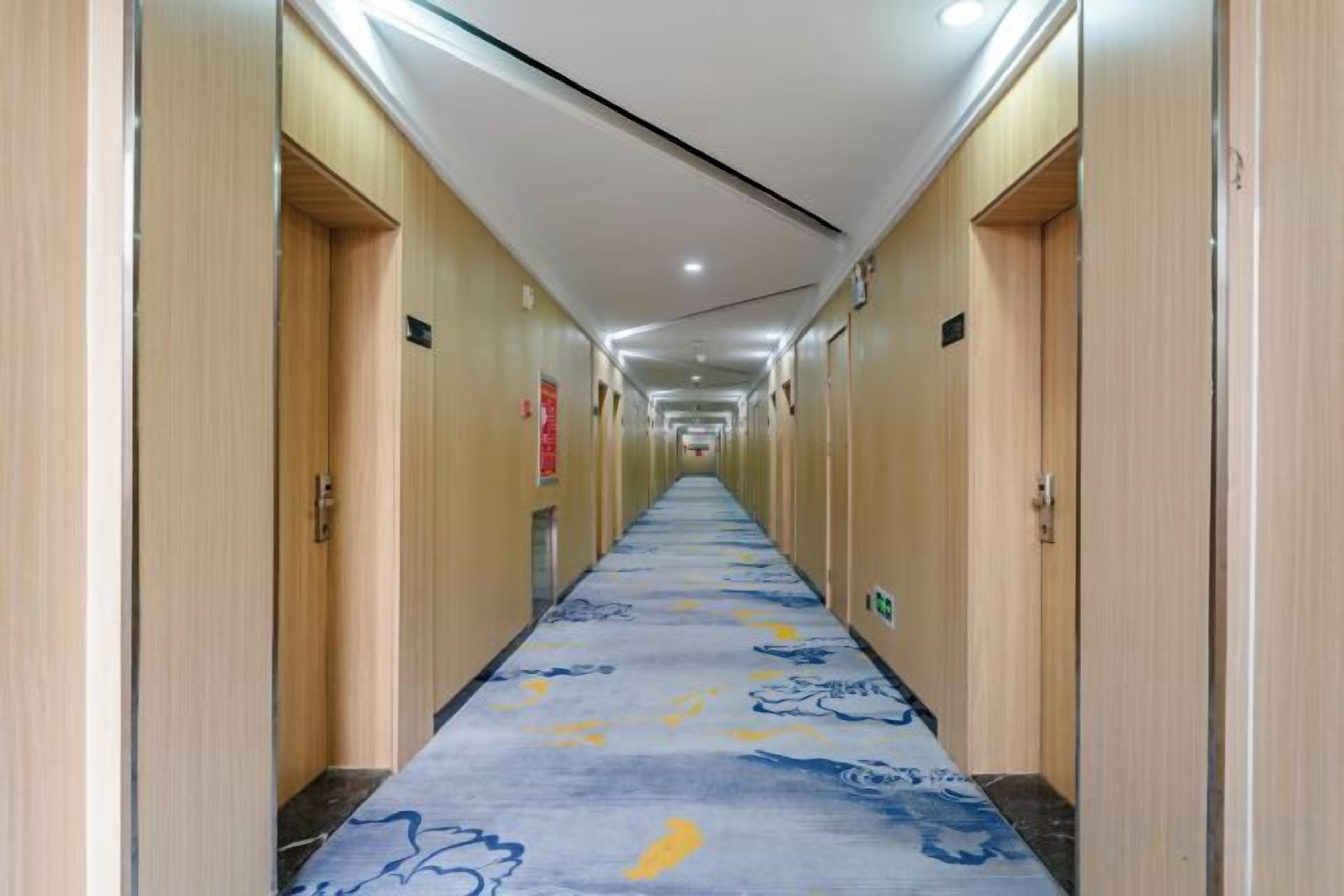 A hotel hallway with wooden doors, a patterned carpet, and overhead lighting.