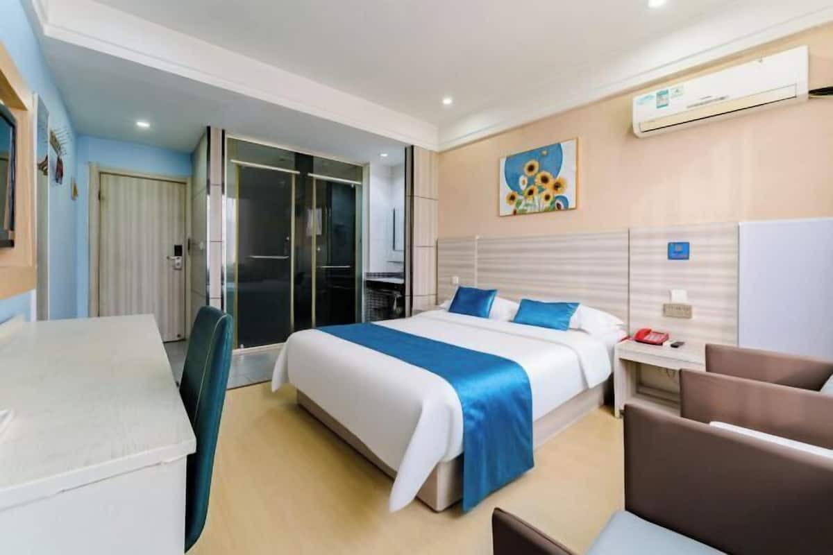 Une chambre d’hôtel avec un lit, un bureau, une chaise, une armoire et un tableau au mur.