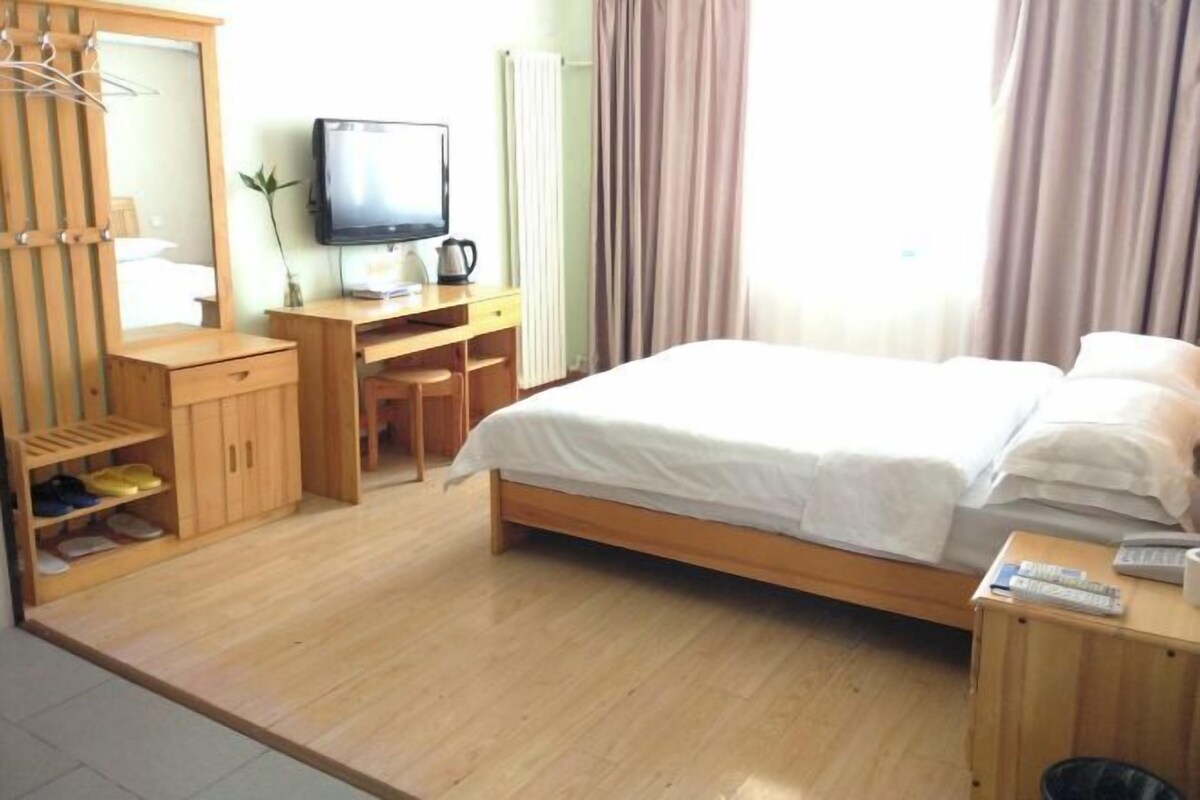 Ein Hotelzimmer mit einem Holzbett, einem Schreibtisch mit Fernseher, einem Spiegel und einem Kleiderschrank.