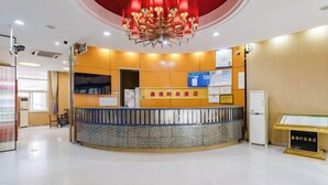 Een receptiegebied van een hotel met een modern design, met een centraal receptiebalie, een kroonluchter en een prikbord met mededelingen.