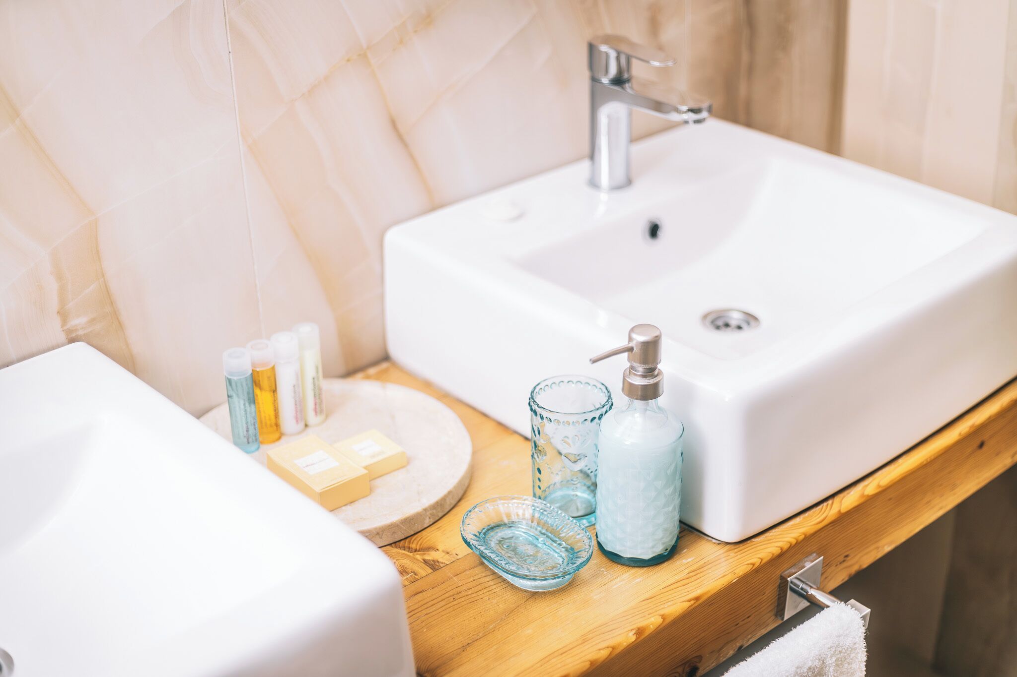 A bathroom with a white sink, a wooden countertop, and toiletries including soap, shampoo, and a bottle of lotion.
