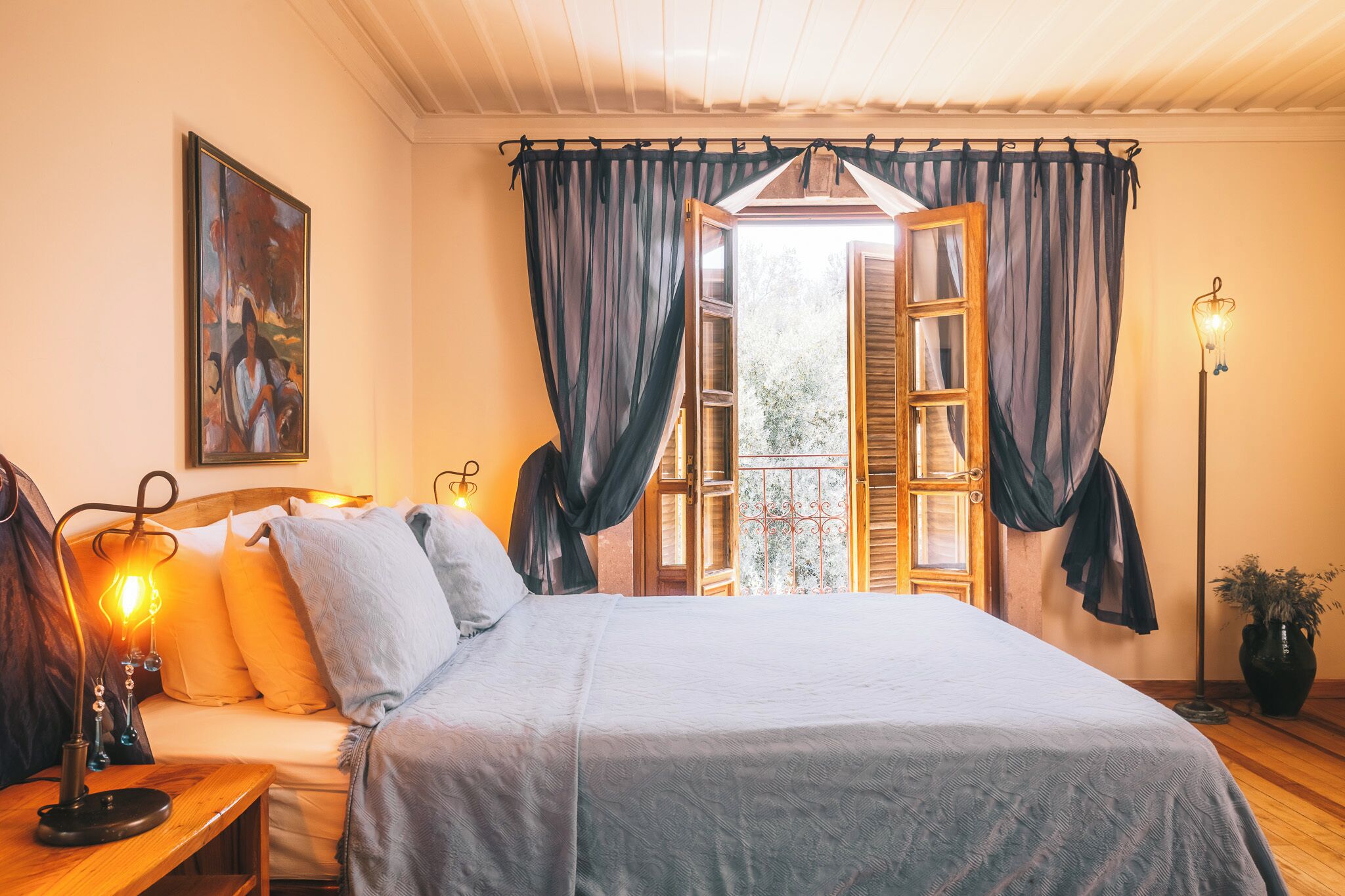 A bedroom with a bed, bedside table, lamp, curtains, and a window with a view.