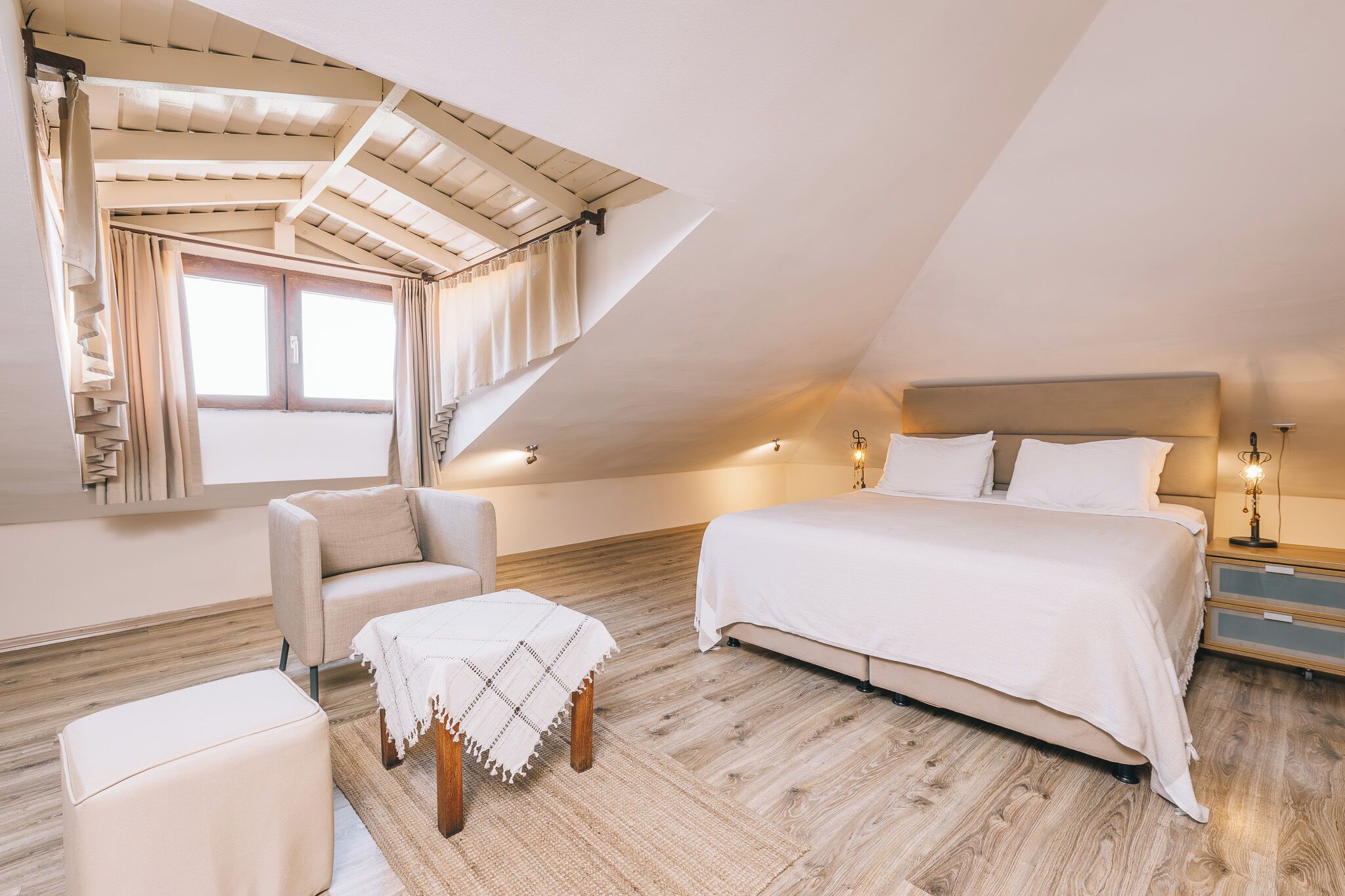 Een slaapkamer met een schuine wand, een bed, een stoel, een klein tafeltje en een nachtkastje met een lamp.