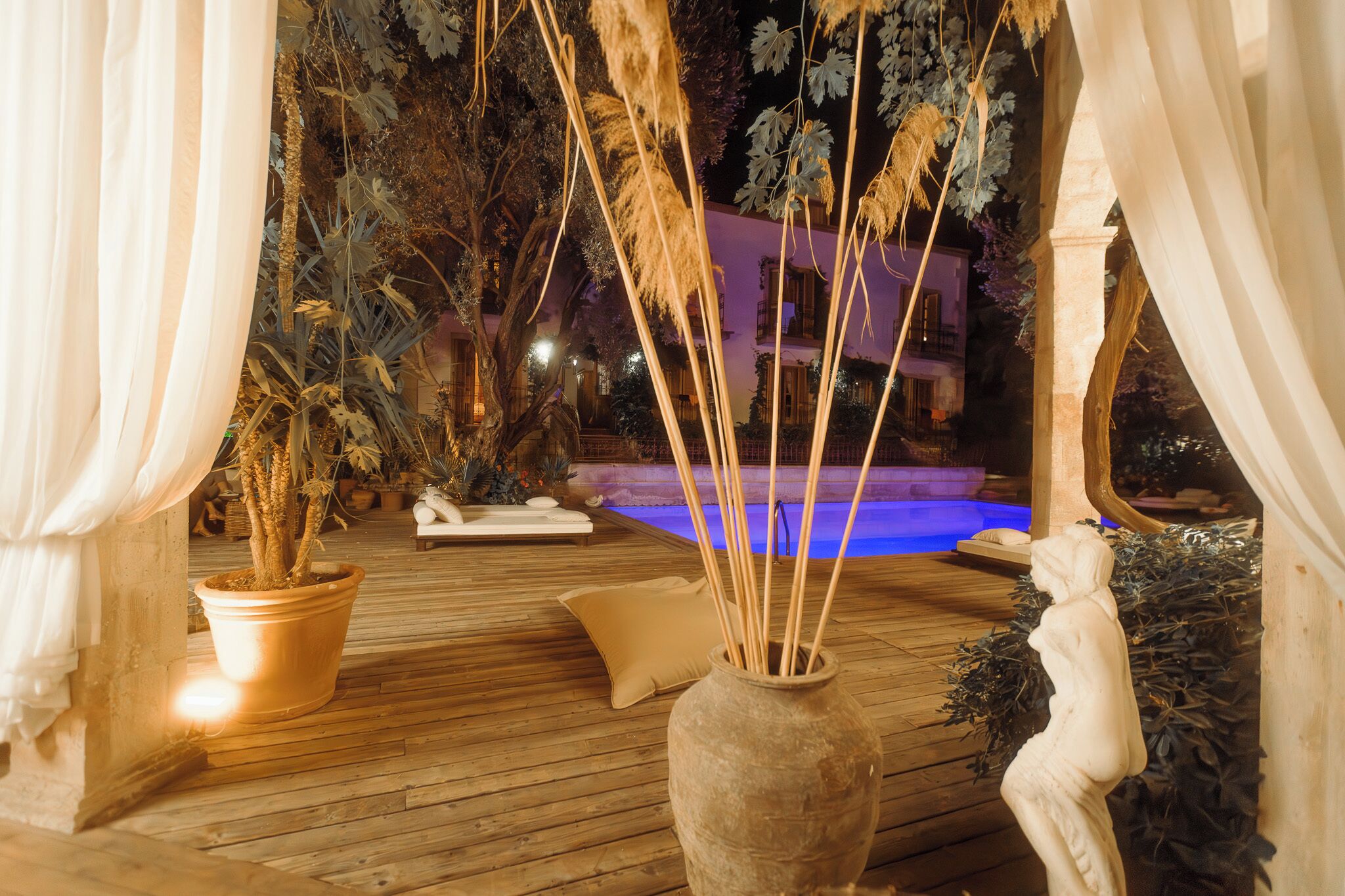 Une terrasse en bois avec un jacuzzi, des plantes en pot et une statue.