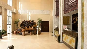 A spacious lobby with a reception desk, a wooden sculpture centerpiece, and potted plants.