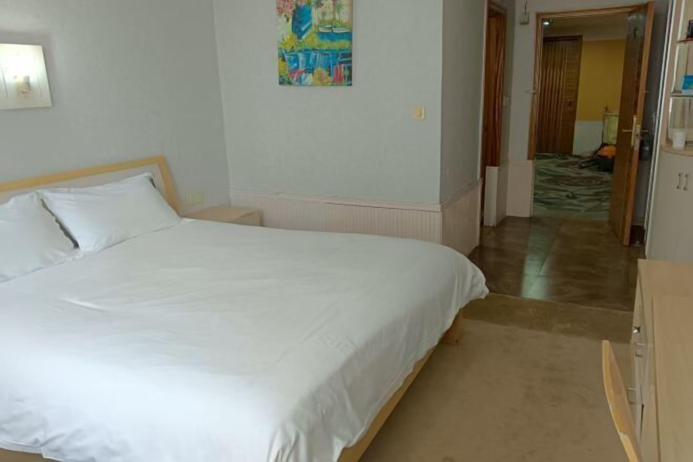 Une chambre à coucher avec un lit, une table de chevet, un tableau au mur et une porte donnant sur une autre pièce.