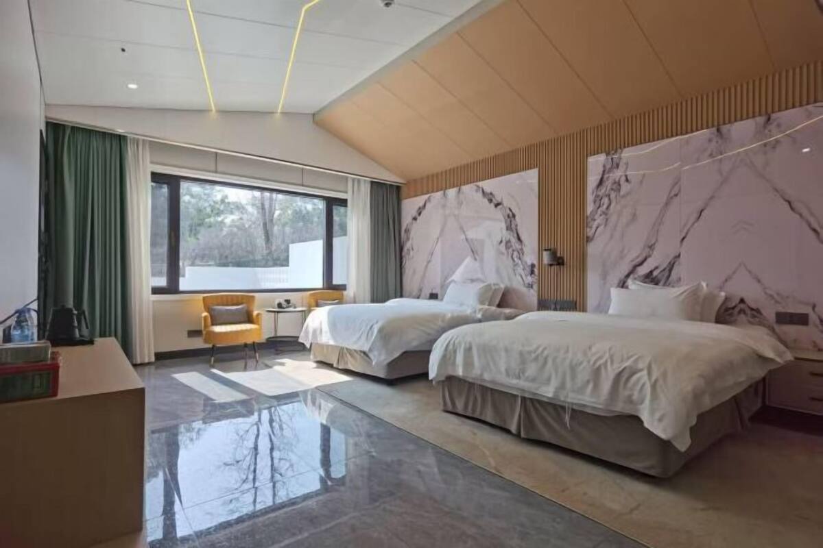 A modern hotel room with two beds, a large window, and a marble accent wall.
