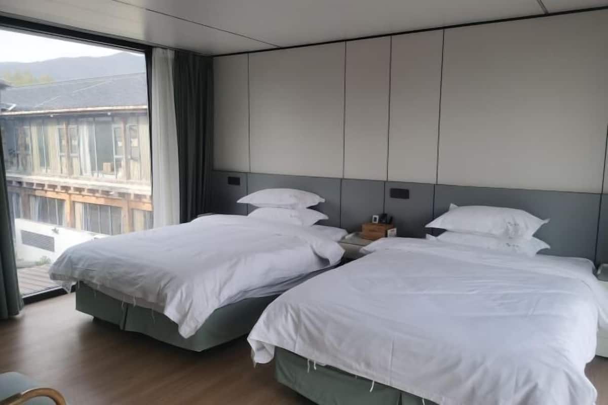 A hotel room with two beds, a large window, and a view of a building outside.