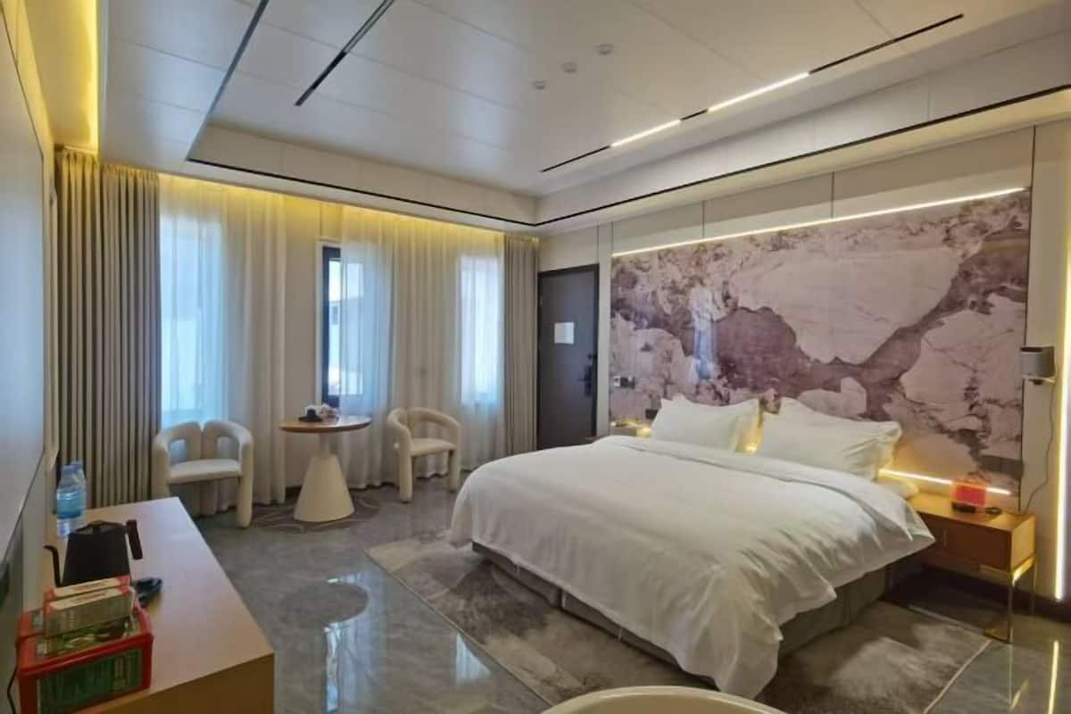 A modern hotel room with a large bed, a desk, two chairs, and a small table.