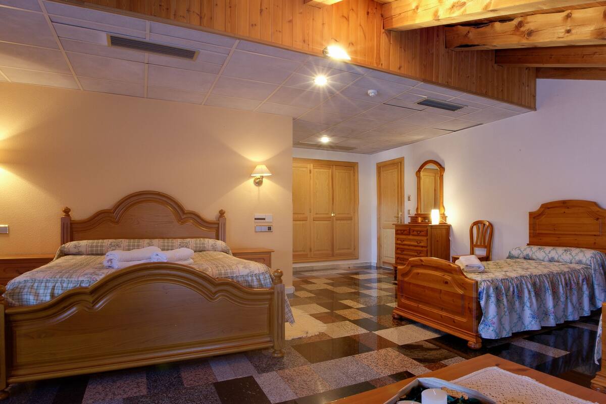 A hotel room with three wooden beds, a checkered floor, and wooden ceiling beams.