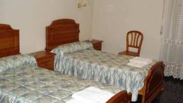 A simple room with two wooden beds, a small table, a chair, and a lamp.