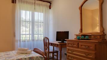 Un dormitorio con una cama, un aparador de madera, un escritorio con una computadora y una ventana con cortinas.