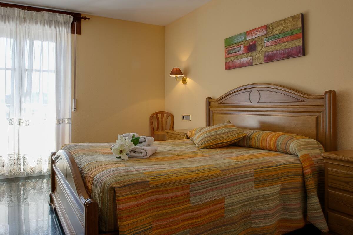 A neatly made bed with a striped bedspread, a wooden headboard, and a wall-mounted painting.