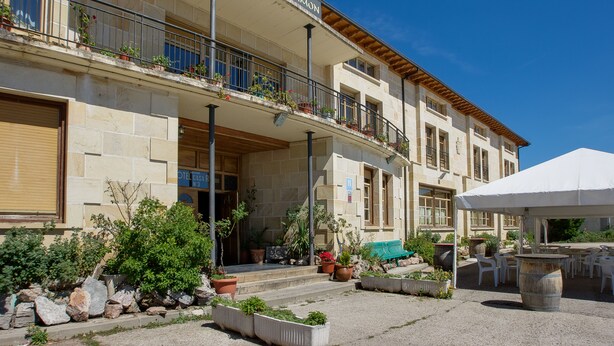 A building with a sign reading "Hostal Casa Ramon". It features a balcony with potted plants, a covered outdoor seating area with tables and chairs, and a stone facade. - Hostal Casa Ramón III (Quintanar de la Sierra)