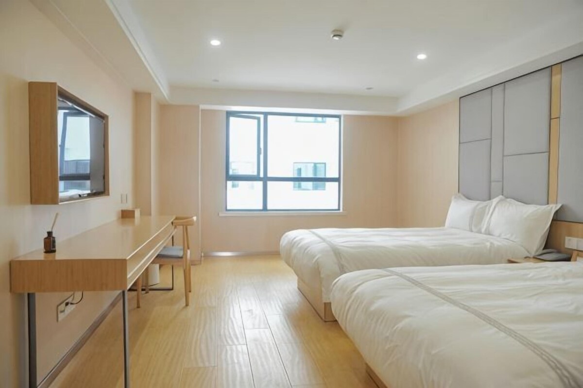 A hotel room with two beds, a desk, a chair, a TV, and a large window.
