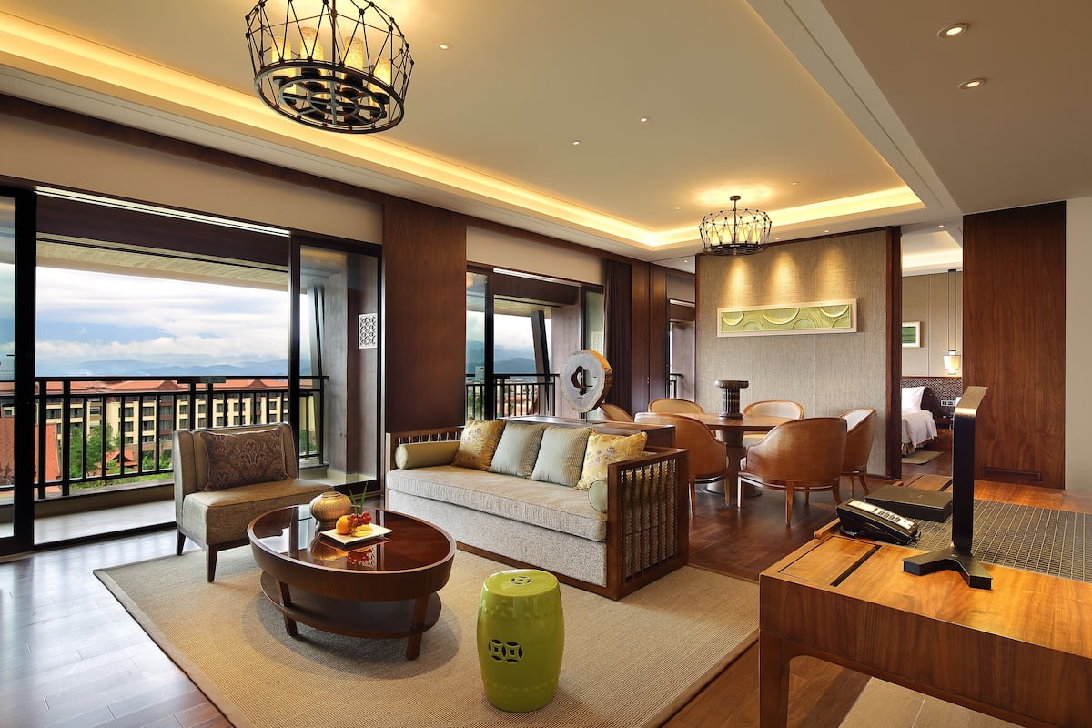 A spacious living room with a sofa, coffee table, and chairs, a piano, and a balcony with a view.