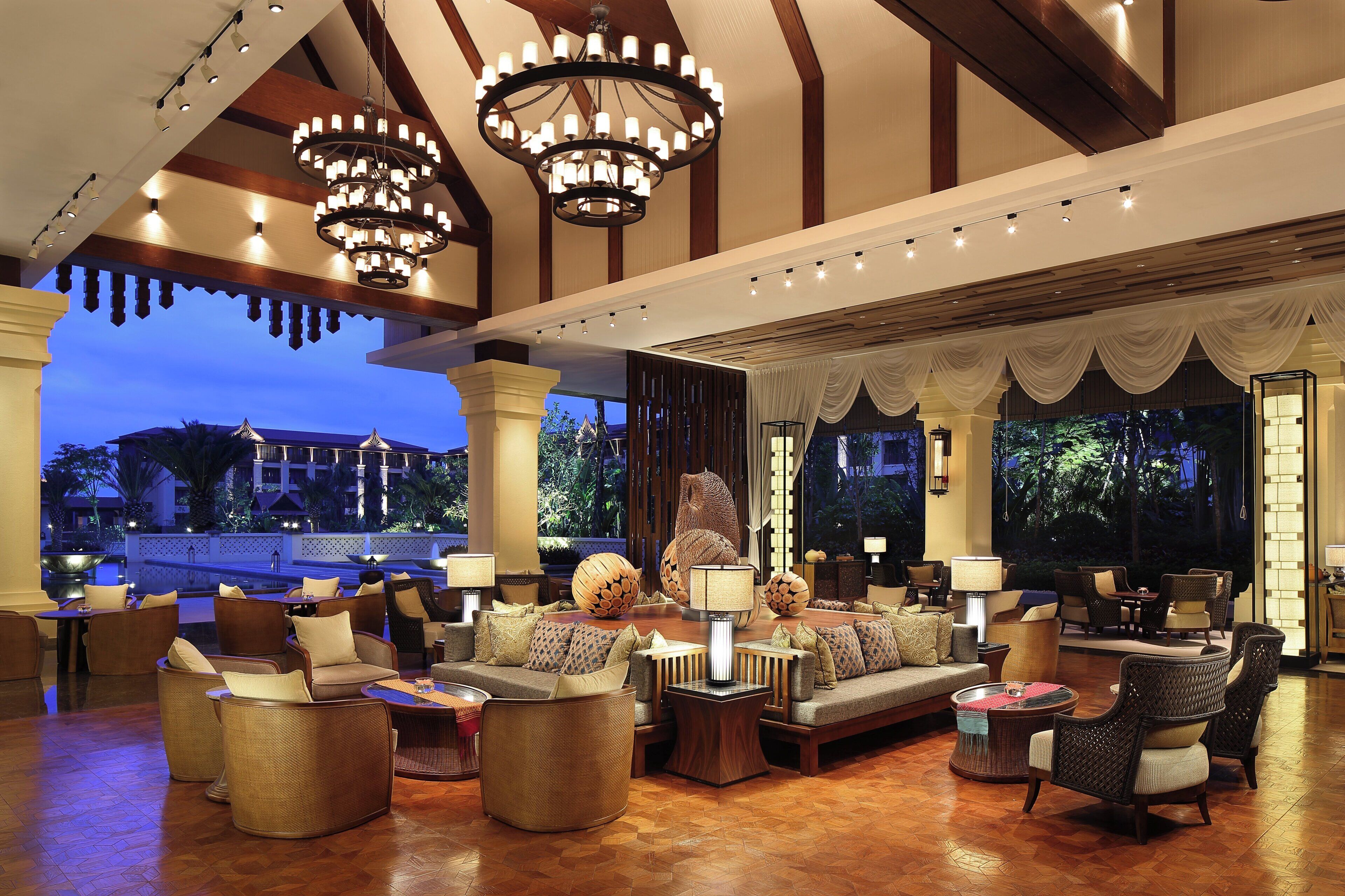 A spacious lounge area with multiple seating options, a large chandelier, and a view of a building and trees.