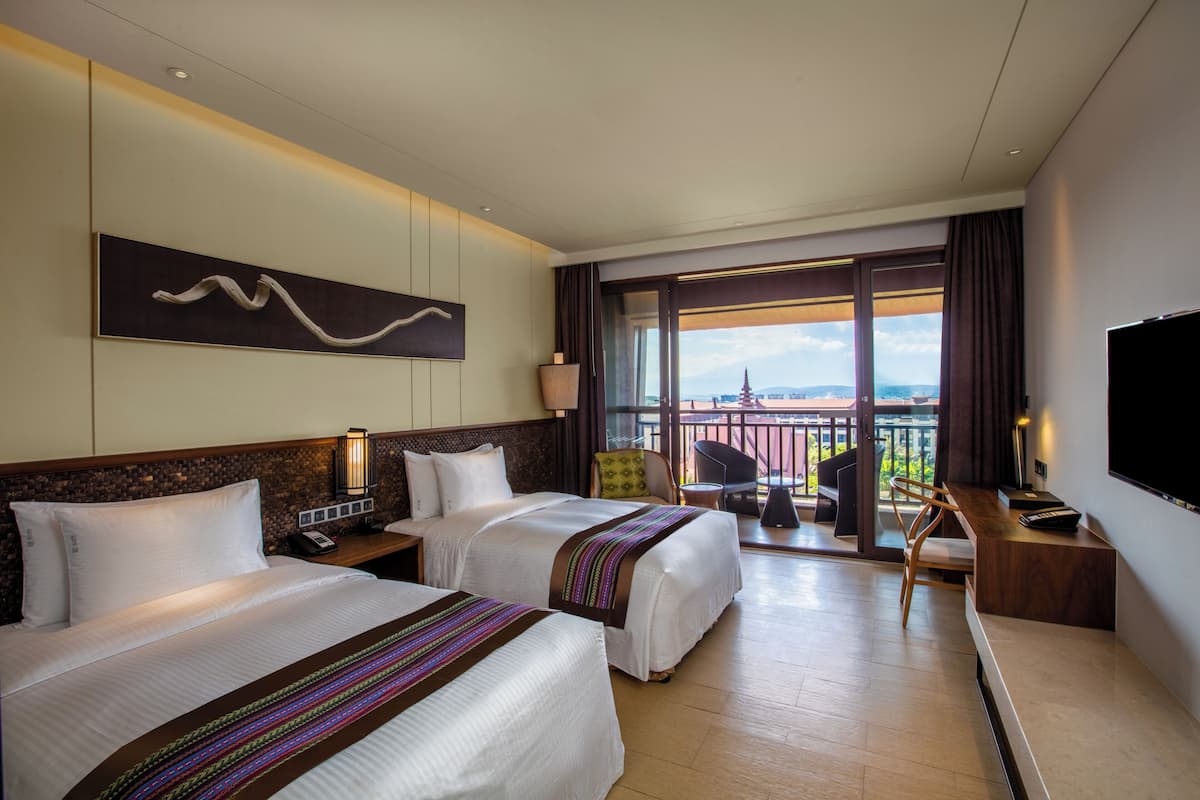 Ein Hotelzimmer mit zwei Betten, einem Fernseher, einem Schreibtisch und einem Balkon mit Blick.
