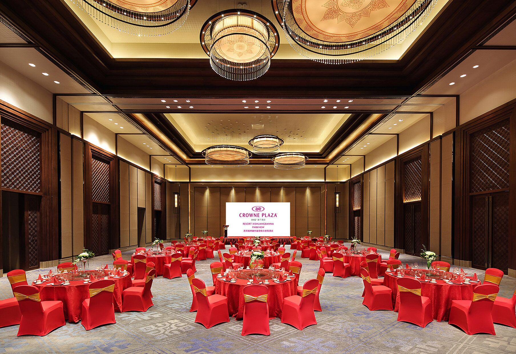 A large ballroom with red tables and chairs, a chandelier, and a sign for Crowne Plaza.