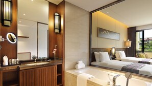 A modern hotel bathroom with a wooden vanity, a large mirror, a bathtub, and a bed with a view of the outdoors. - Crowne Plaza Resort Xishuangbanna Parkview by IHG (Xishuangbanna Dai)