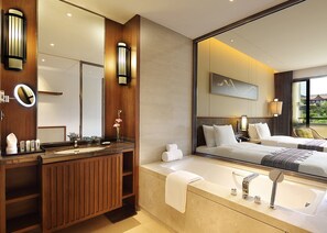 Uma casa de banho de hotel moderna com toucador de madeira, um espelho grande, uma banheira e uma cama com vista para o exterior.