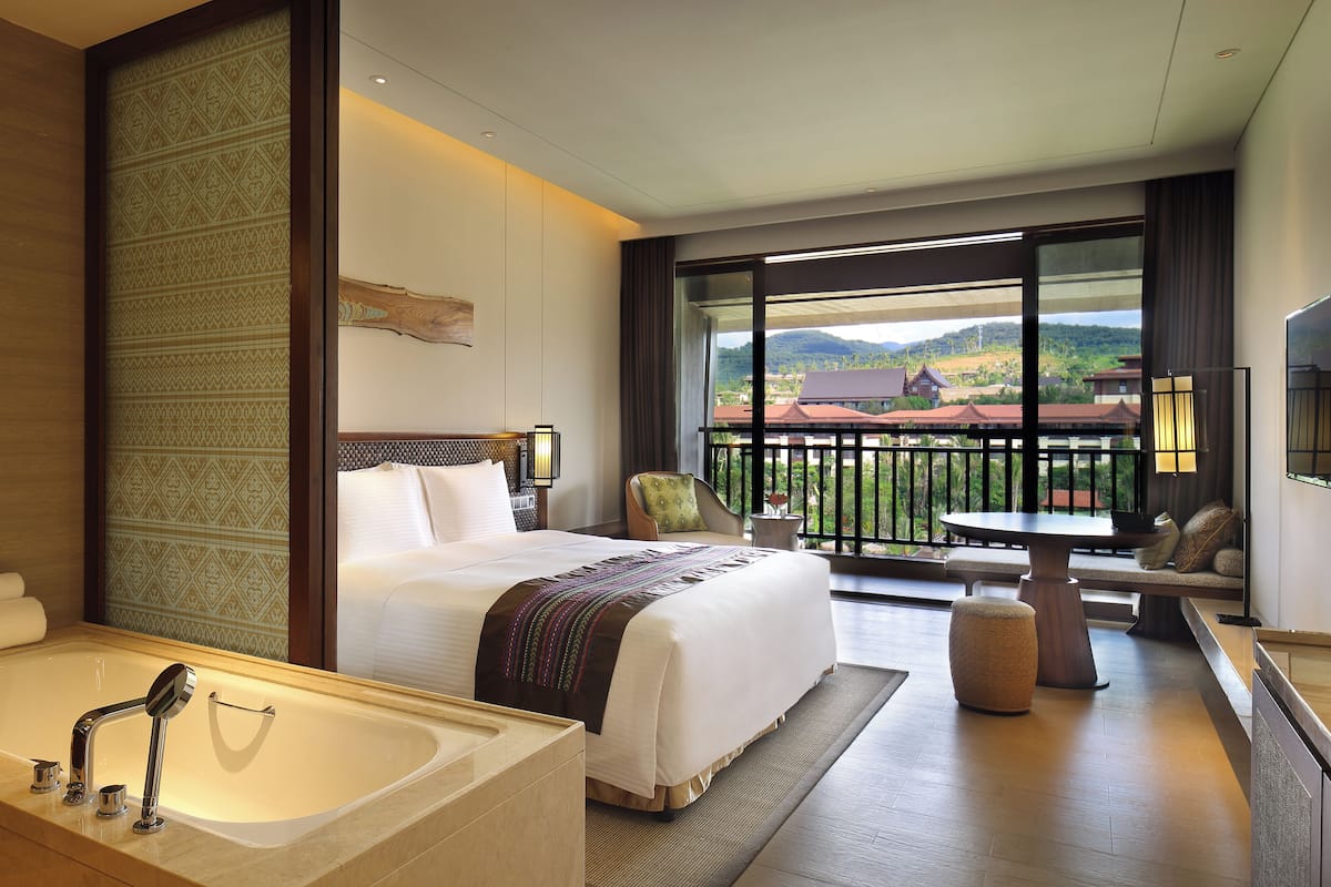 Ein Hotelzimmer mit einem großen Bett, einer Badewanne, einem Balkon mit Bergblick und einem Essbereich.