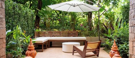 A patio with a wooden bench, a round table, and an umbrella.
