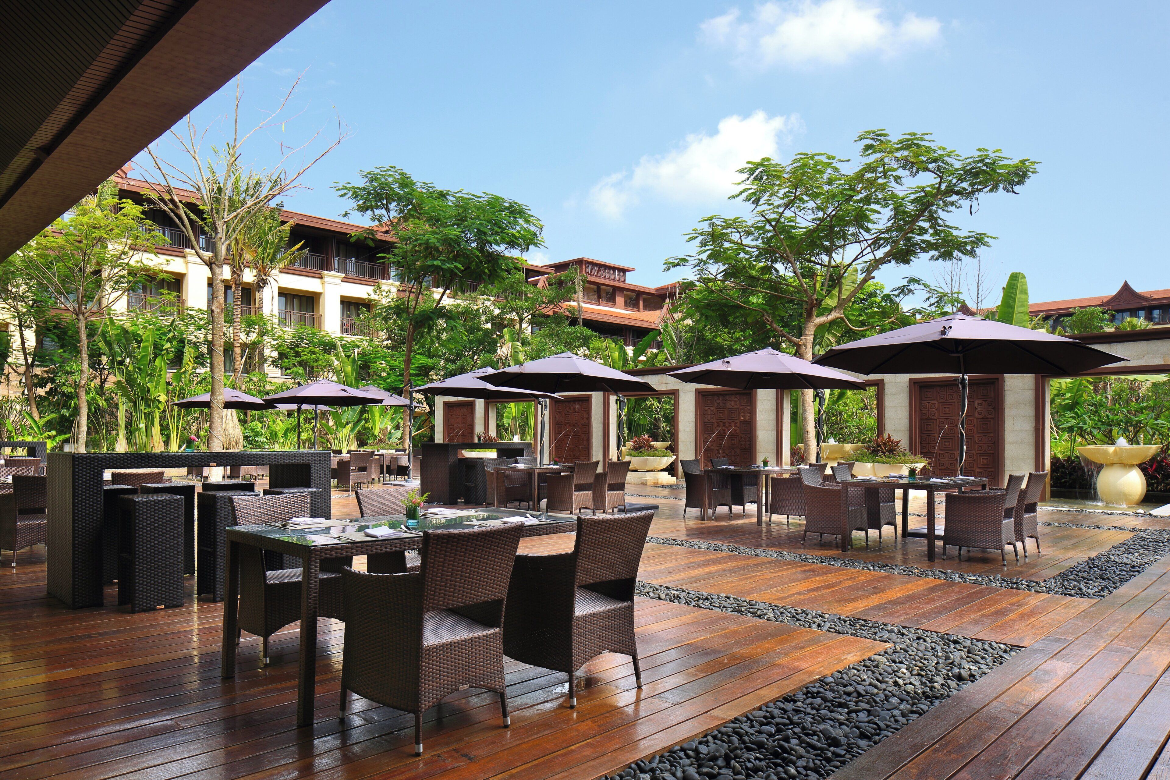 An outdoor patio area with tables and chairs, umbrellas, and a view of a building in the background.