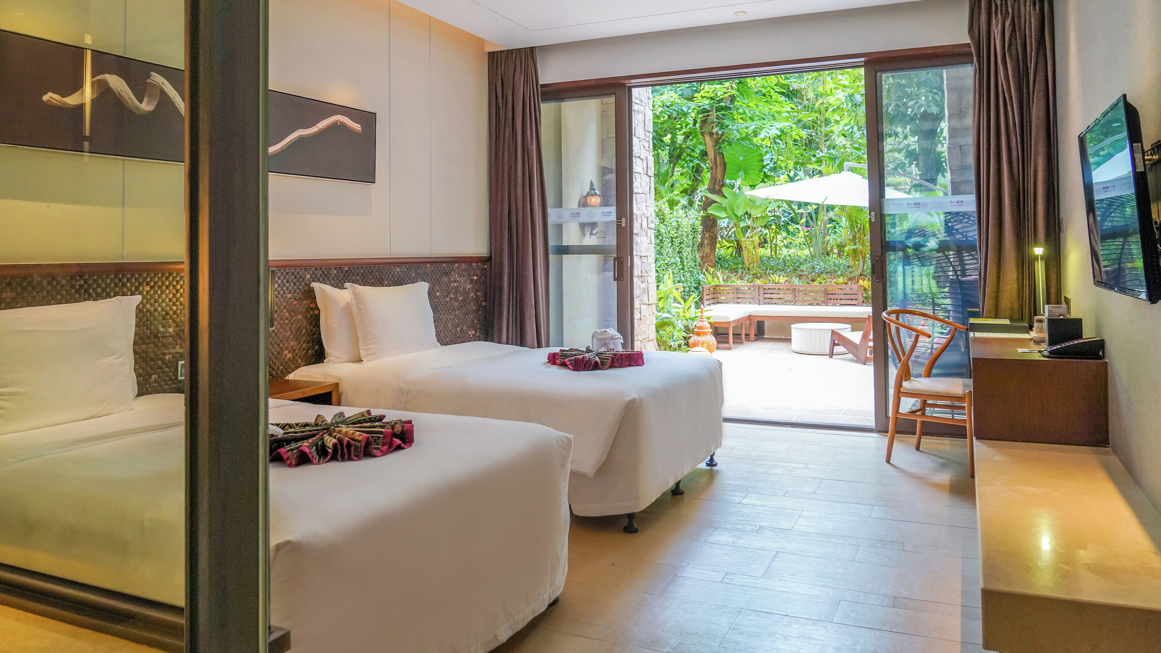 A hotel room with two beds, a desk, a chair, and a view of the garden.