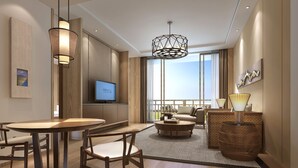 A modern hotel room with a large window, a flat-screen TV, a dining area with a round table and chairs, a sofa, and a decorative lamp. - Crowne Plaza Resort Xishuangbanna Parkview by IHG (Xishuangbanna Dai)