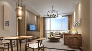A modern hotel room with a large window, a flat-screen TV, a dining area with a round table and chairs, a sofa, and a decorative lamp. - Crowne Plaza Resort Xishuangbanna Parkview by IHG (Xishuangbanna Dai)
