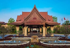 Um edifício tradicional tailandês com entrada central, rodeado por um jardim ajardinado com fontes.